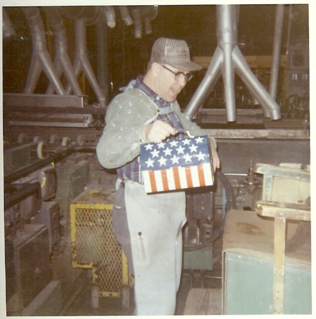 Factory worker holding lunch pail, decorated with stars and stripes.